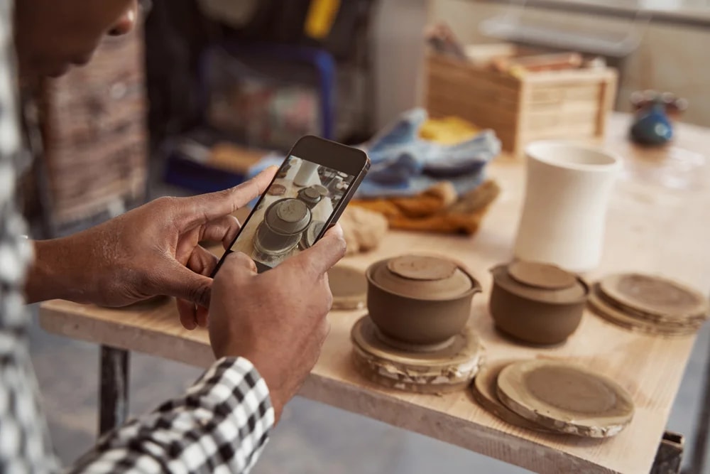 Artesano fotografiando piezas de cerámica con el celular para subirlas a su tienda